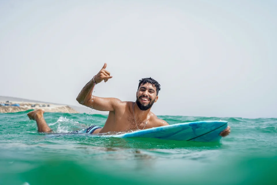 Surfer smiling and making a shaka sign on a surfboard in emerald ocean water