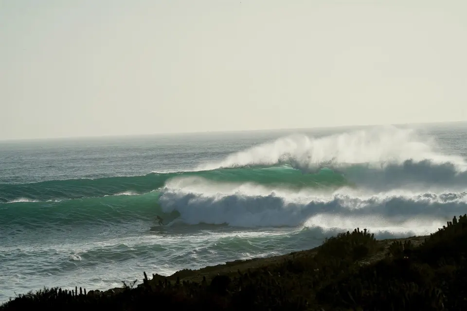 Wide in-water view of a glassy morning set wave breaking on the coast