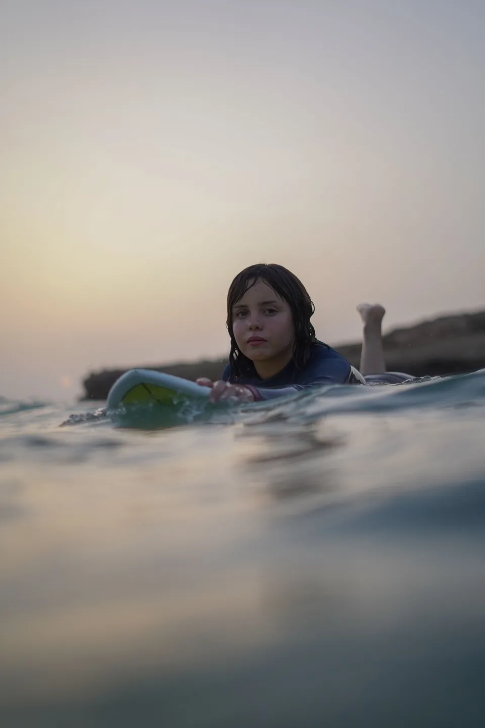 Surfer resting on a board watching the horizon at sunset