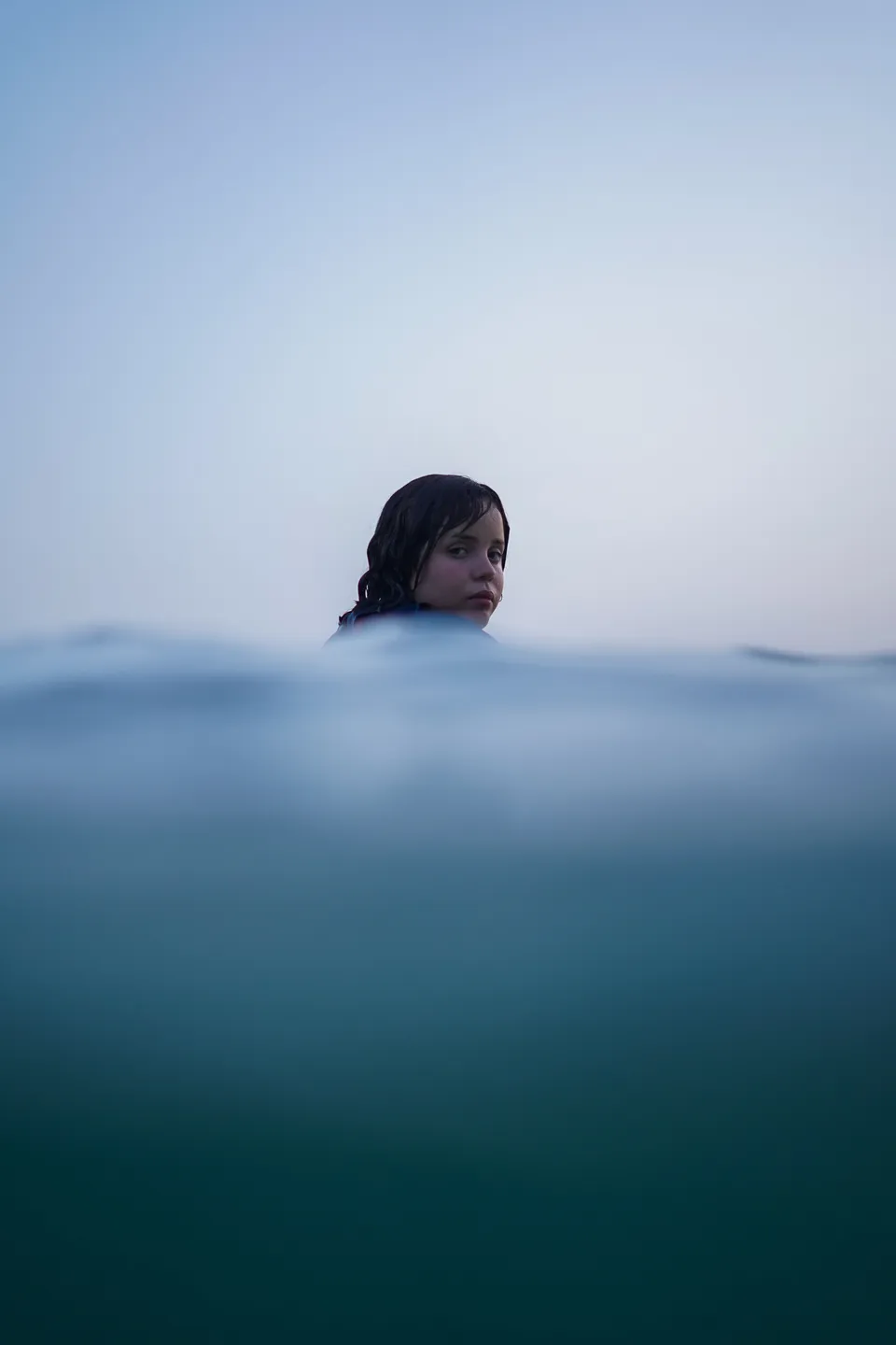 Half-underwater portrait of a surfer at blue hour