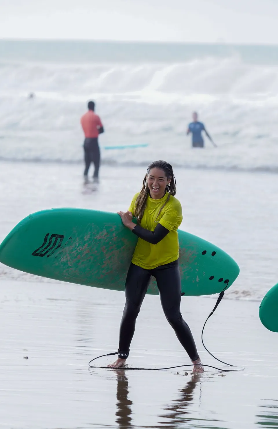Smiling surfer carrying a green board out of the water
